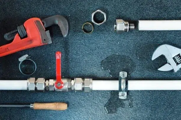 A leaky pipe surrounded by plumbing tools, such as a wrench and a screwdriver