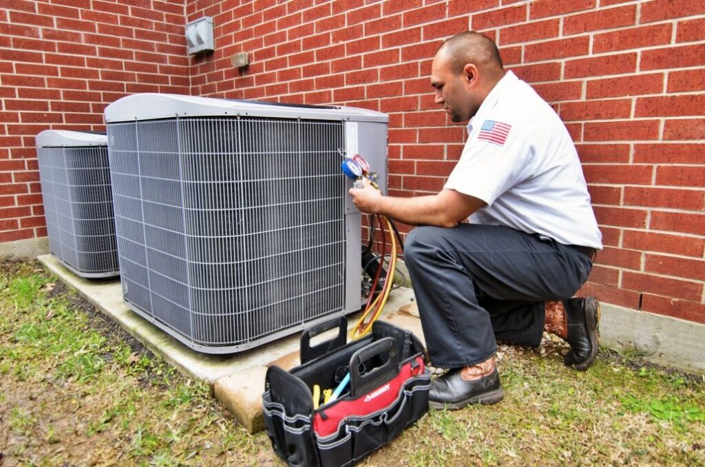 An AC technician is kneeling beside an outdoor AC unit, performing a tune-up.