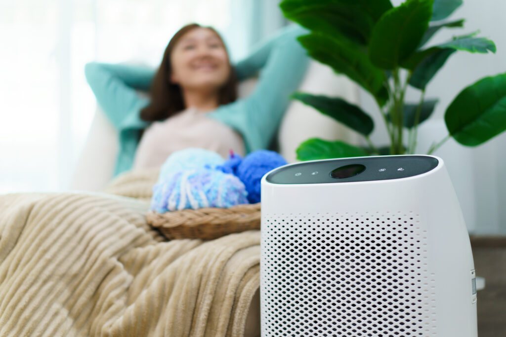 Happy homeowner relaxing in a living room chair while a high-efficiency air purifier is on